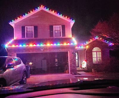 A house is decorated with christmas lights and a car is parked in front of it.