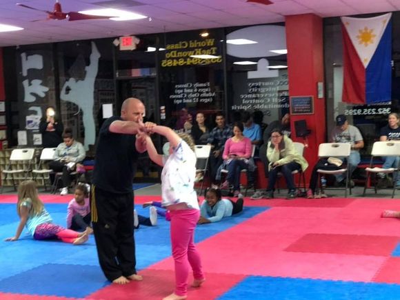 An instructor teaches a young student a self-defense move in a taekwondo studio with a Philippine flag on the wall.
