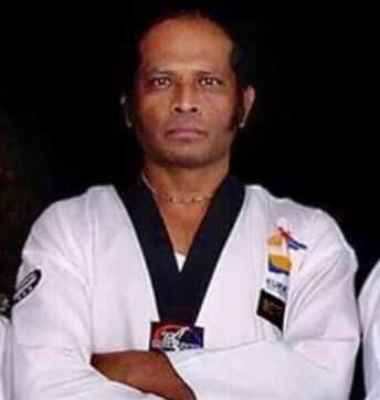 Man looking forward in a martial arts uniform in a stance pose.