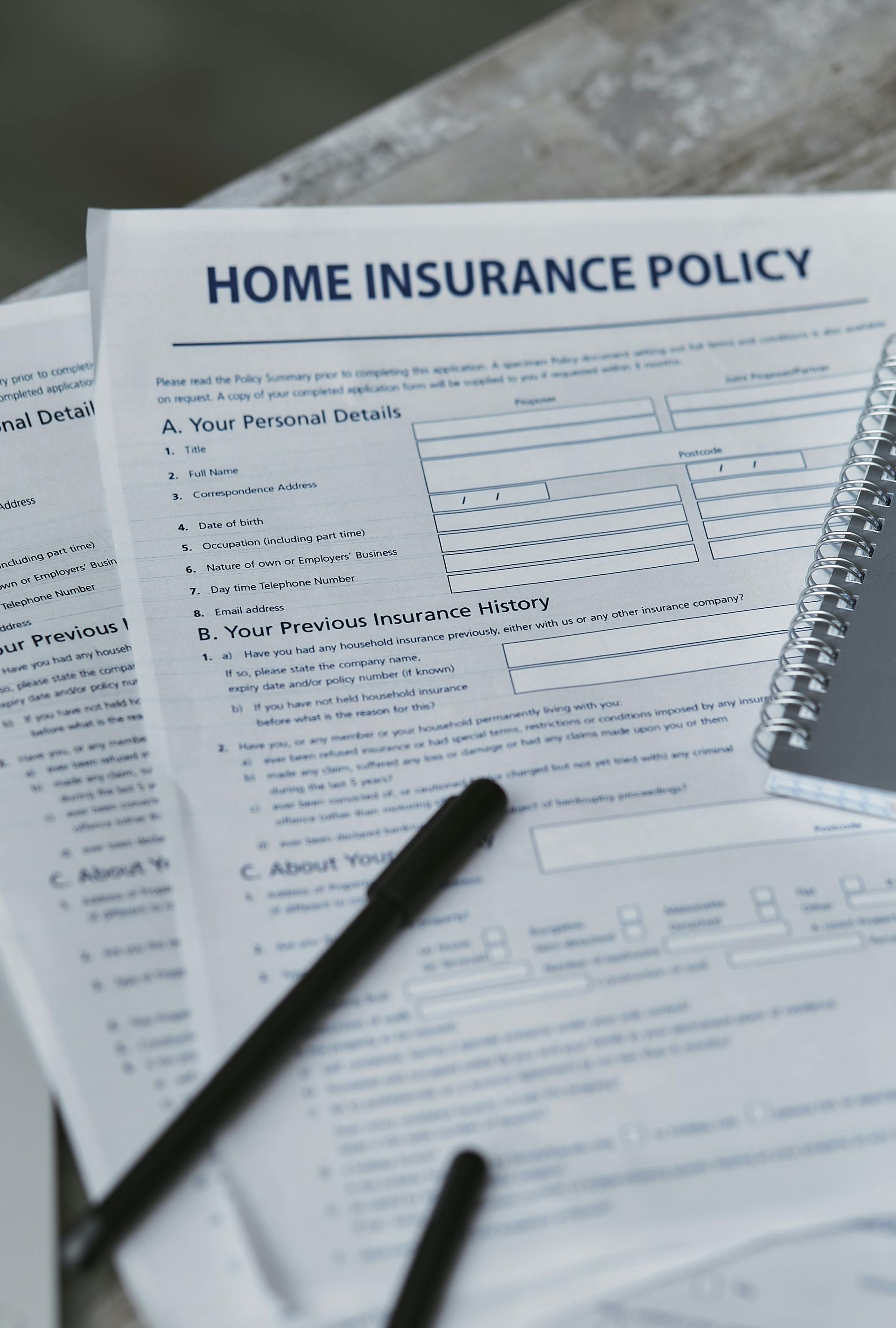Home insurance policy form with a pen and notepad on a wooden surface.