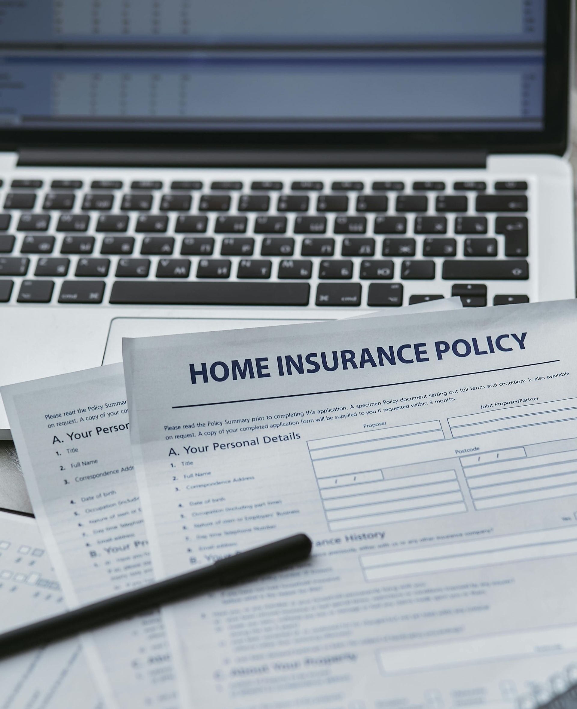 Home insurance policy forms on a desk with a laptop and pen.
