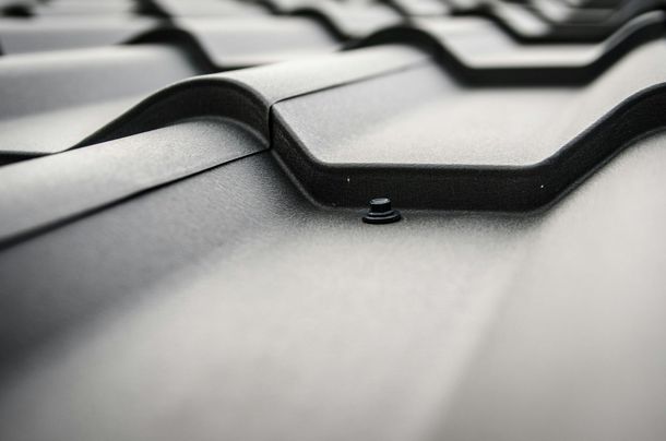 Close-up of a black metal roof with overlapping tiles and a visible fastener.