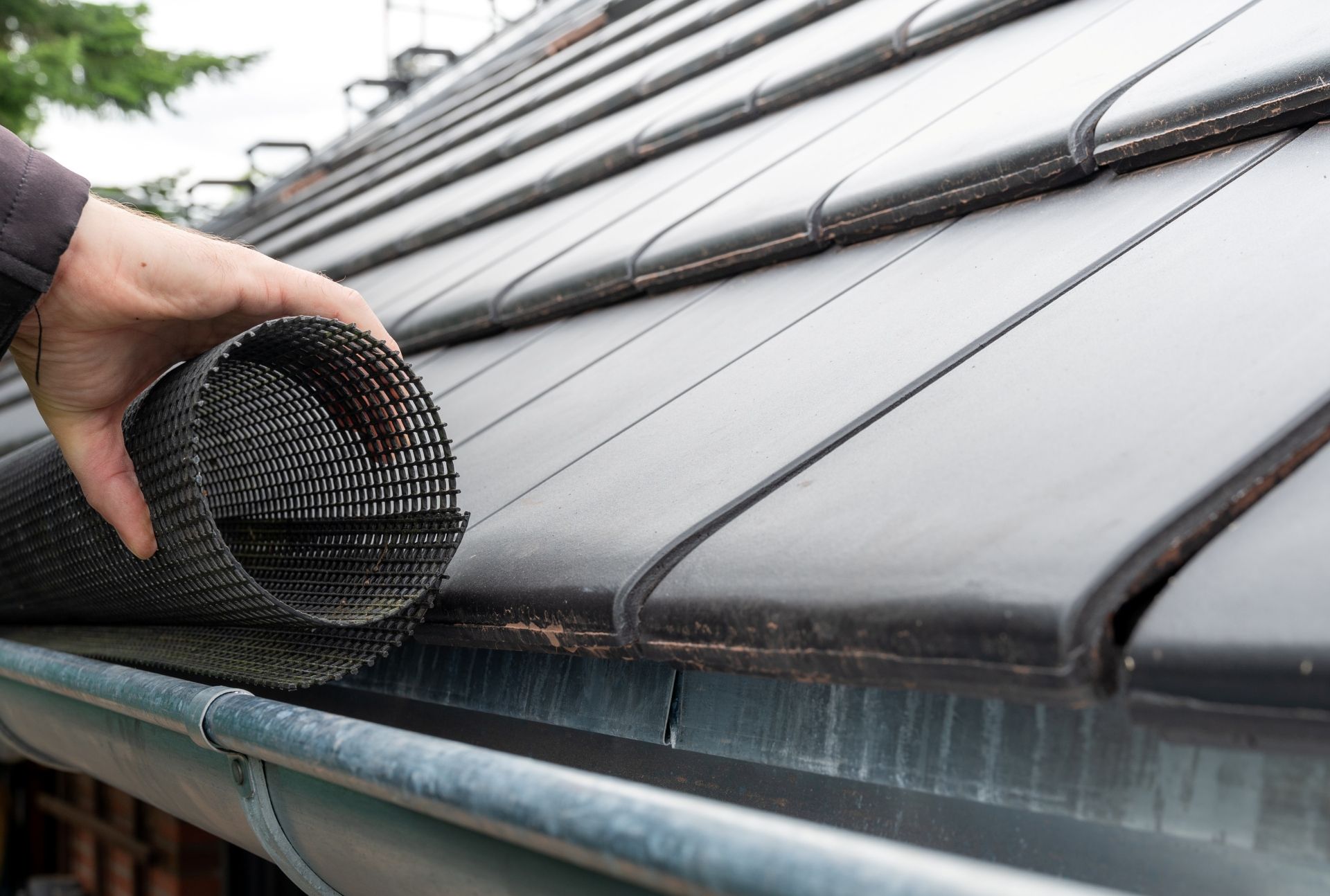 Hand installing black gutter guard on roof tiles.