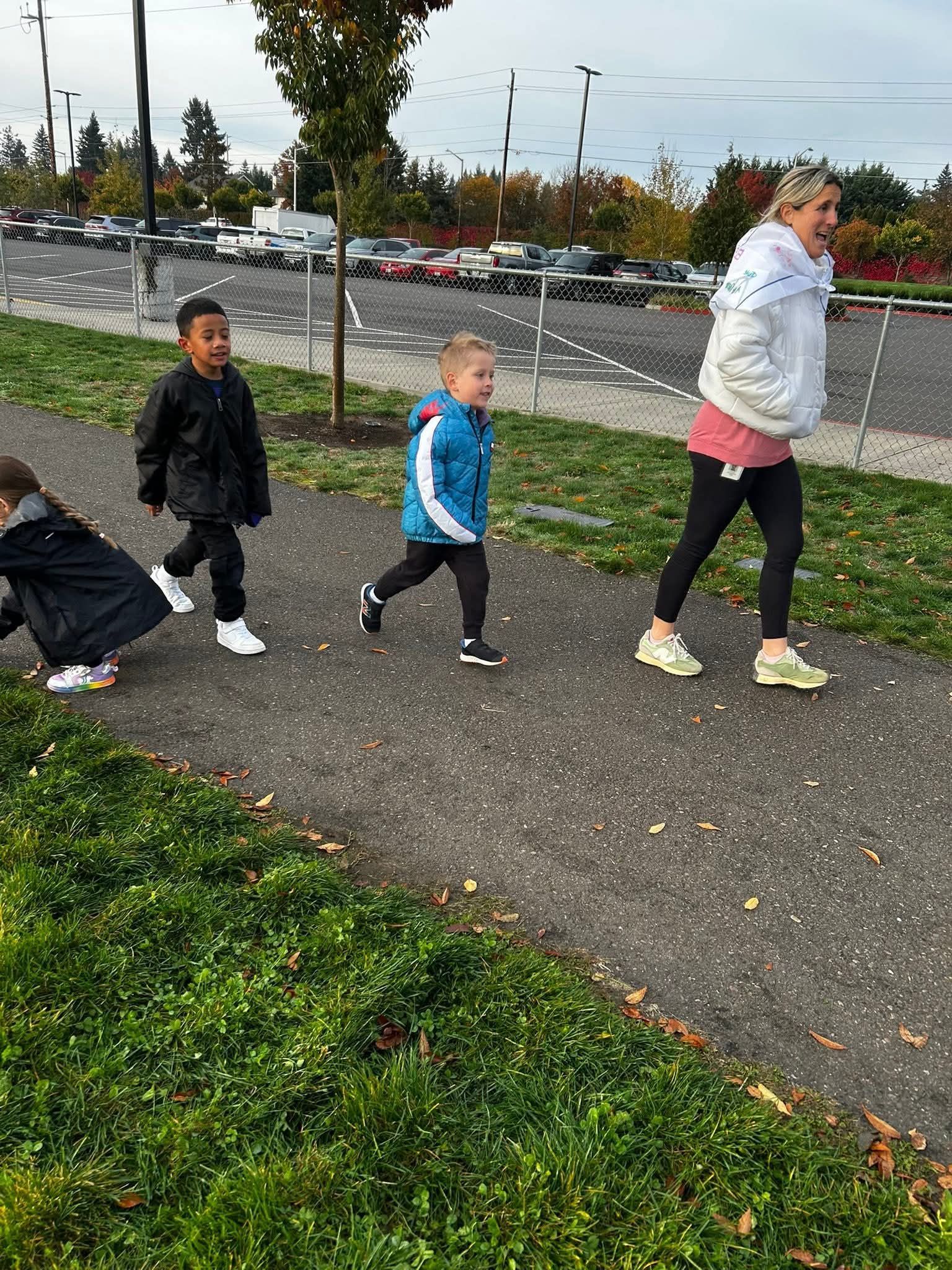 Three children and an adult walking on a path. One child looks back. Overcast day.