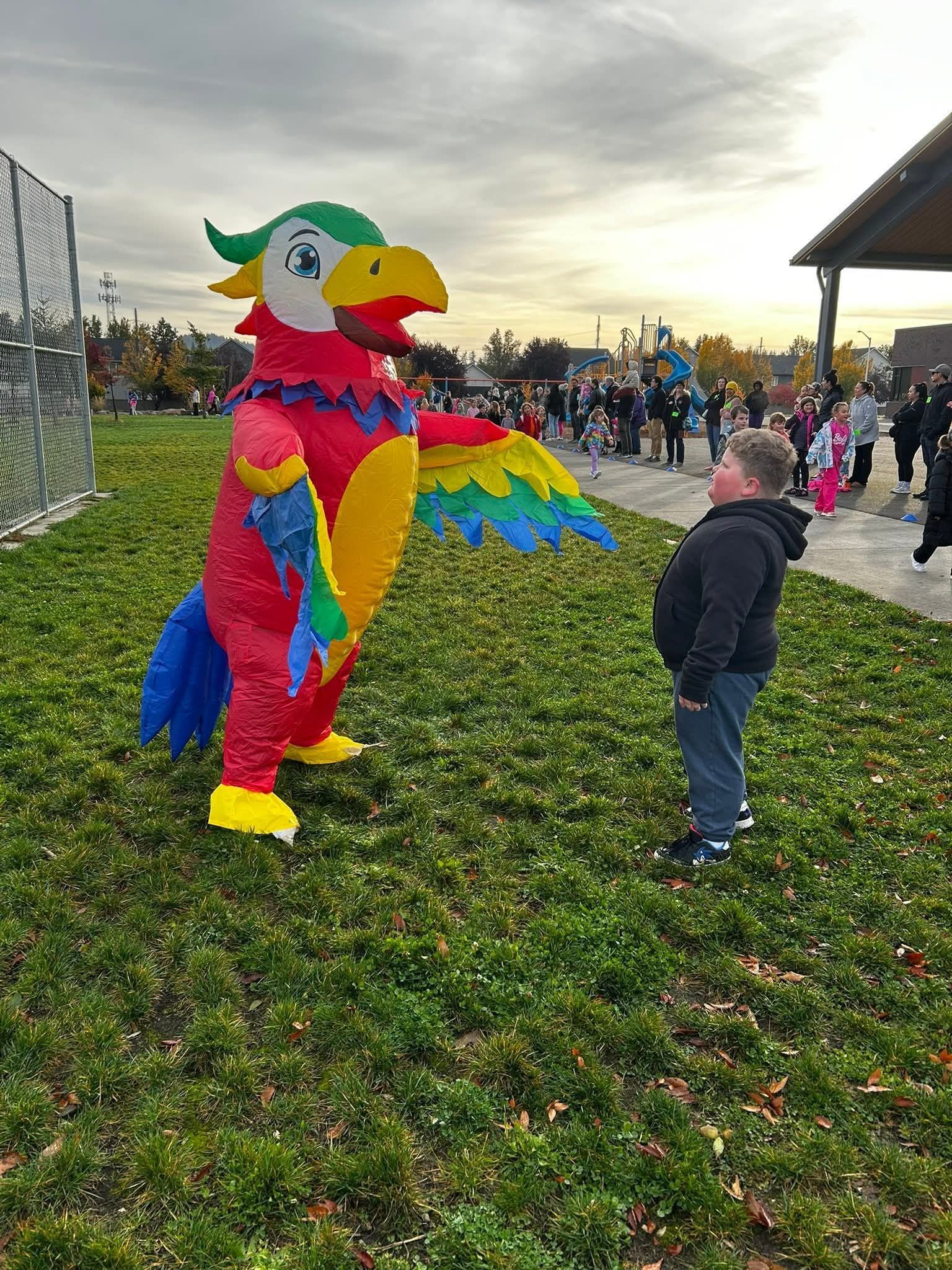 A boy gazes at a large, colorful parrot sculpture made of toy bricks outdoors.