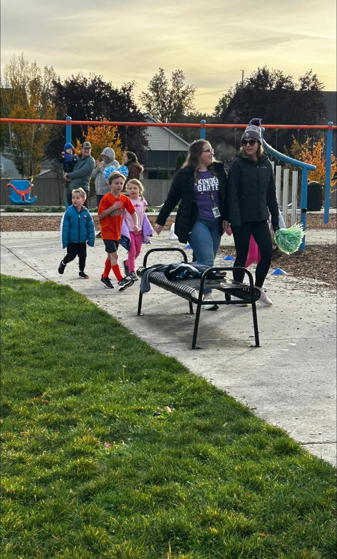 People walking with children in a park near playground equipment.