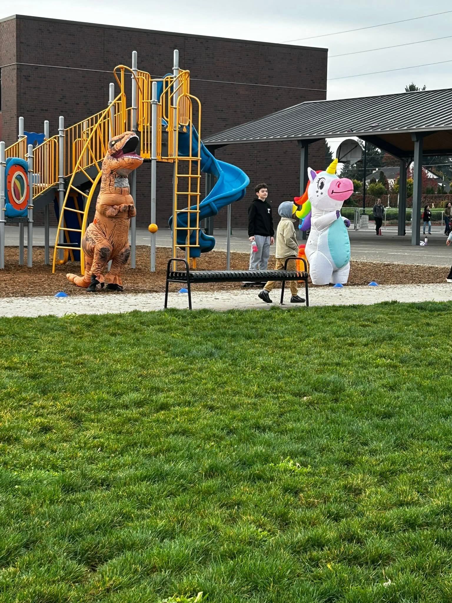 Playground with dinosaur and unicorn inflatables; people nearby; cloudy sky.
