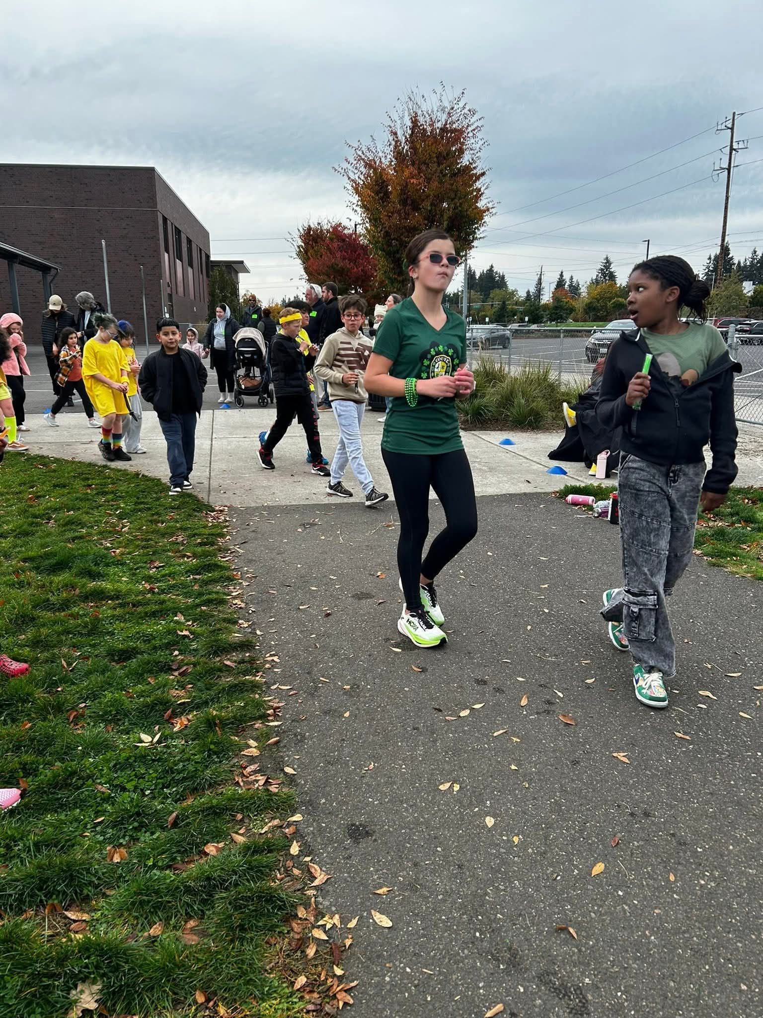 People walking on a path outdoors; one wearing a green shirt, others in the background. Overcast day.