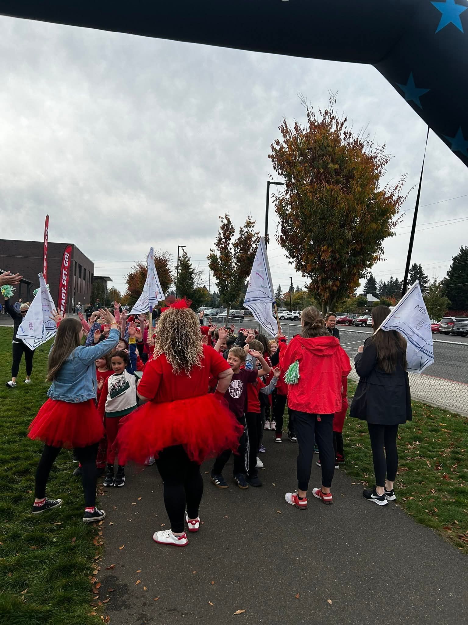 People in red outfits waving flags on a path near a building and trees.
