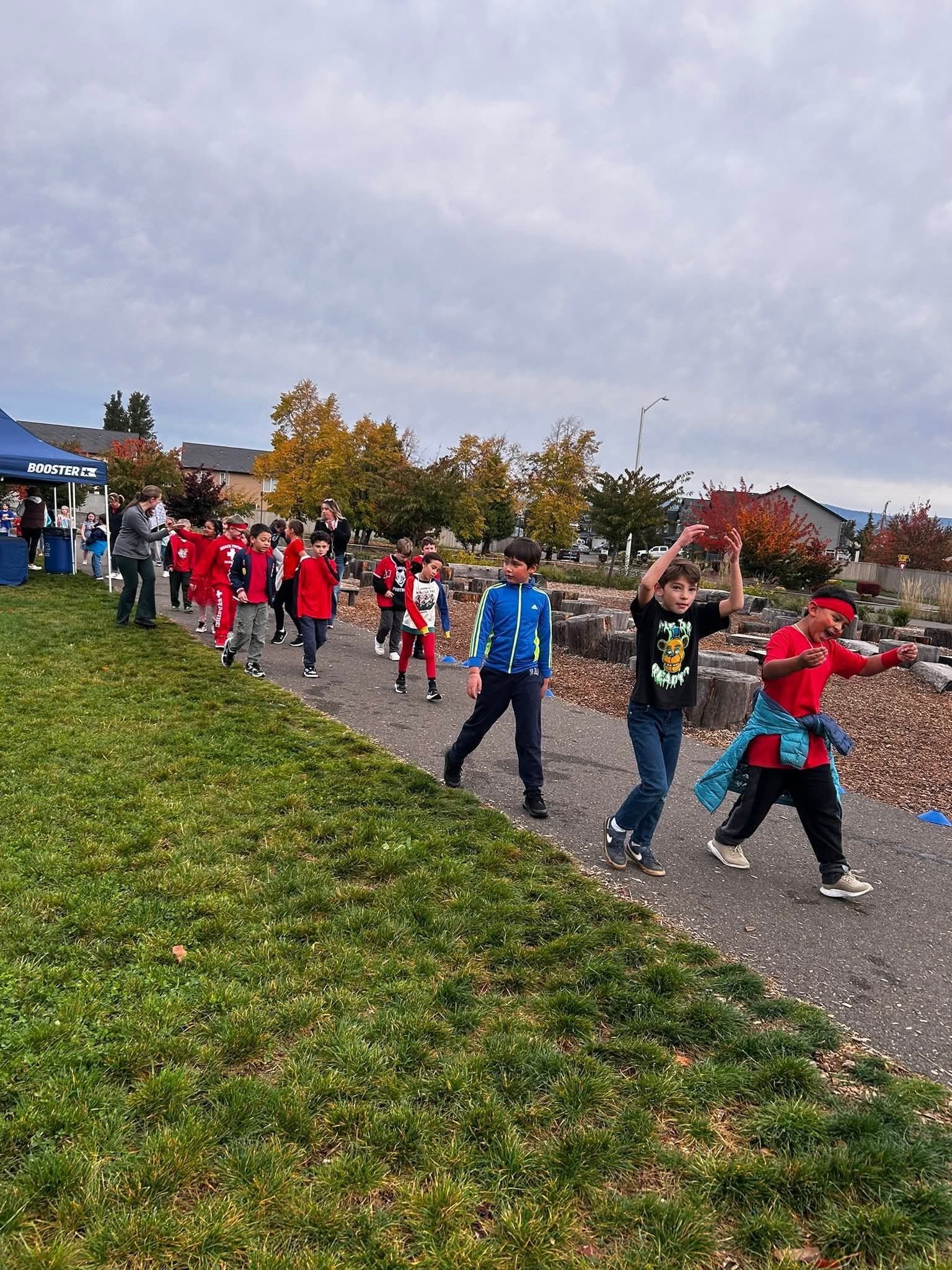 Children walking and running along a path, some wearing red, others in blue, under a cloudy sky.