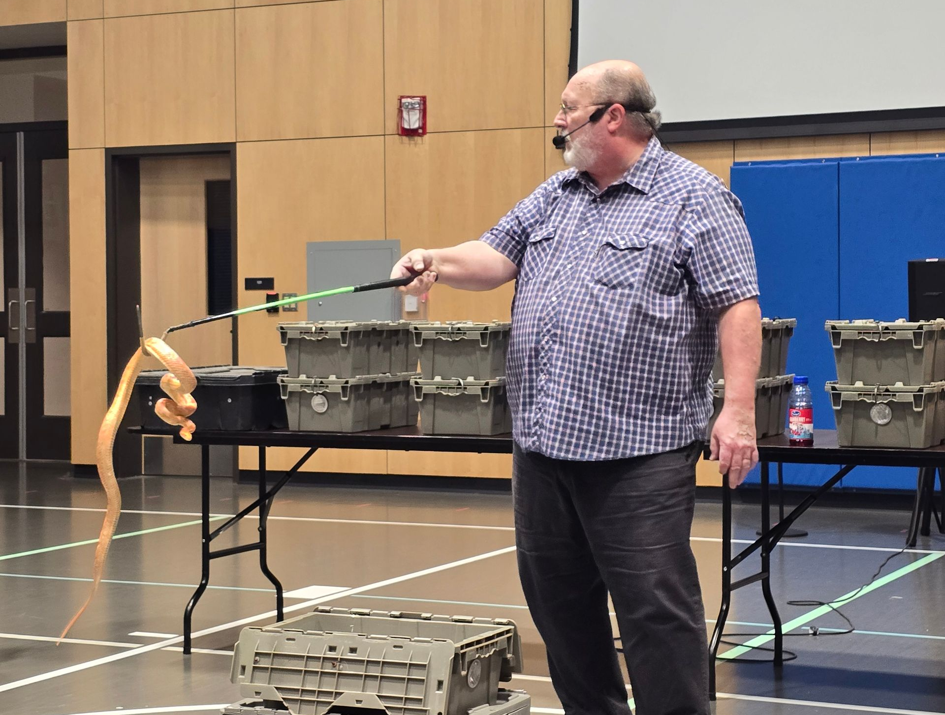 Man with microphone and snake on a stick, giving a presentation in a room with containers.