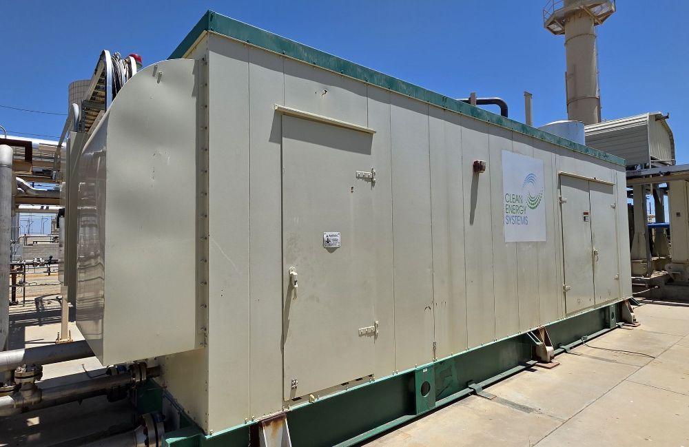 Large beige industrial equipment unit on a metal base beside piping under a blue sky