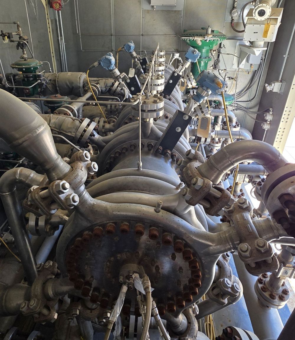 Industrial machinery with large pipes, valves, and a central circular component in a mechanical room