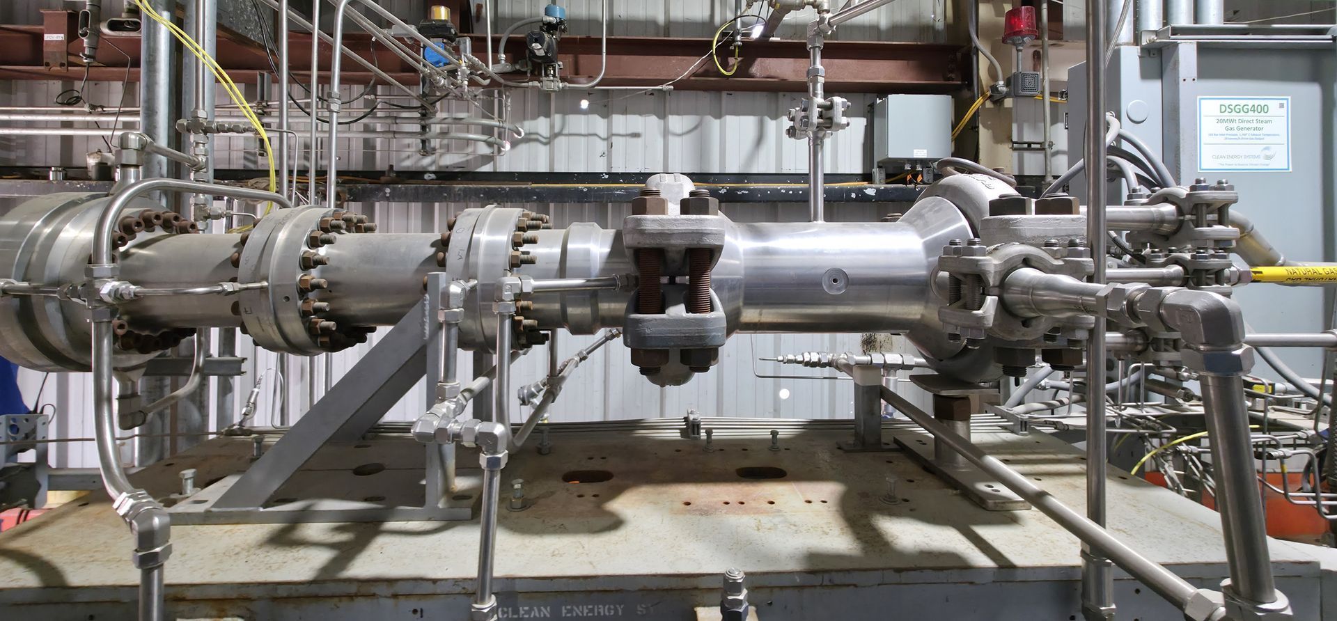 Industrial stainless steel piping and valves in a factory, with a large cylindrical vessel in the foreground