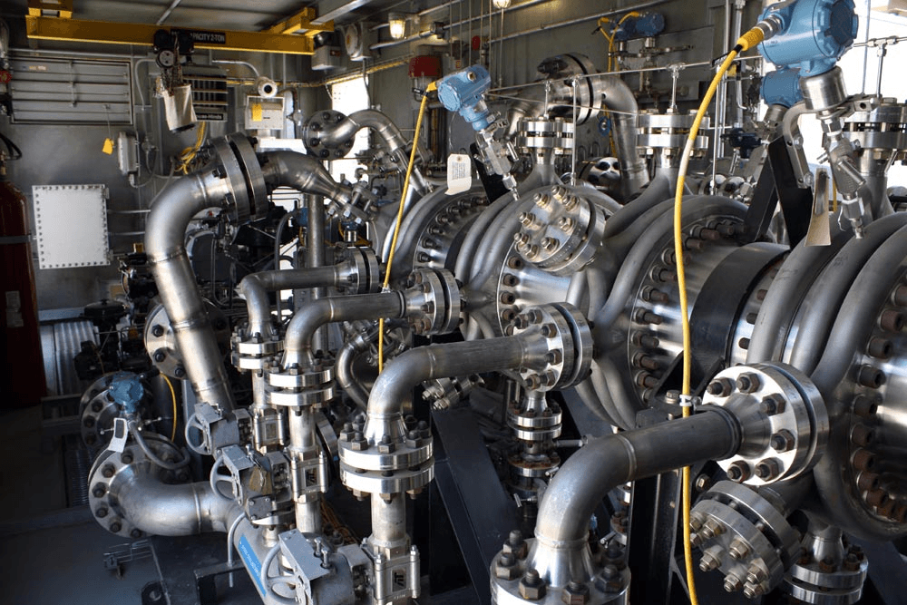 Industrial machinery with metal pipes, valves, and blue components in a factory setting