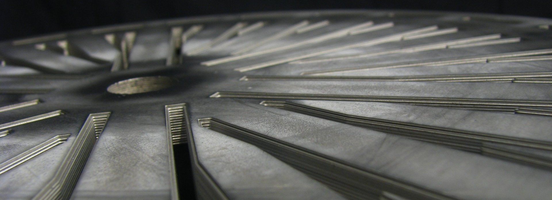 Close-up of a metal wheel hub with radial spokes, shot from a low angle in grayscale.