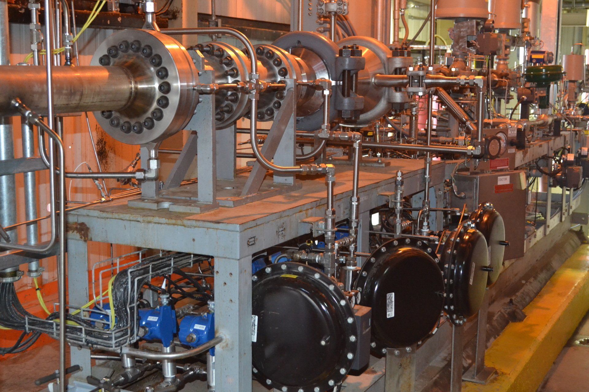 Industrial machine room with shiny metal piping, valves, and large black components on a factory floor