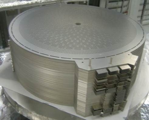 Large circular metallic industrial component with stacked layers and visible internal parts on the side