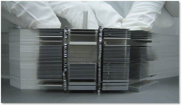 Stacked glass panes with metal brackets being handled by gloved workers in a factory setting
