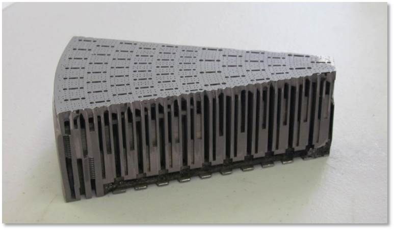 Gray geometric sculpture with rows of vertical black slits on a white surface