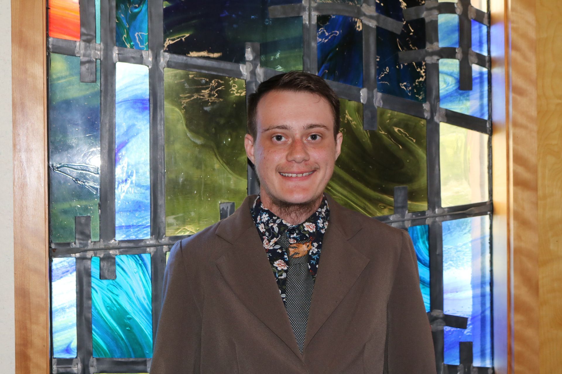 A woman wearing glasses is smiling in front of a stained glass window.