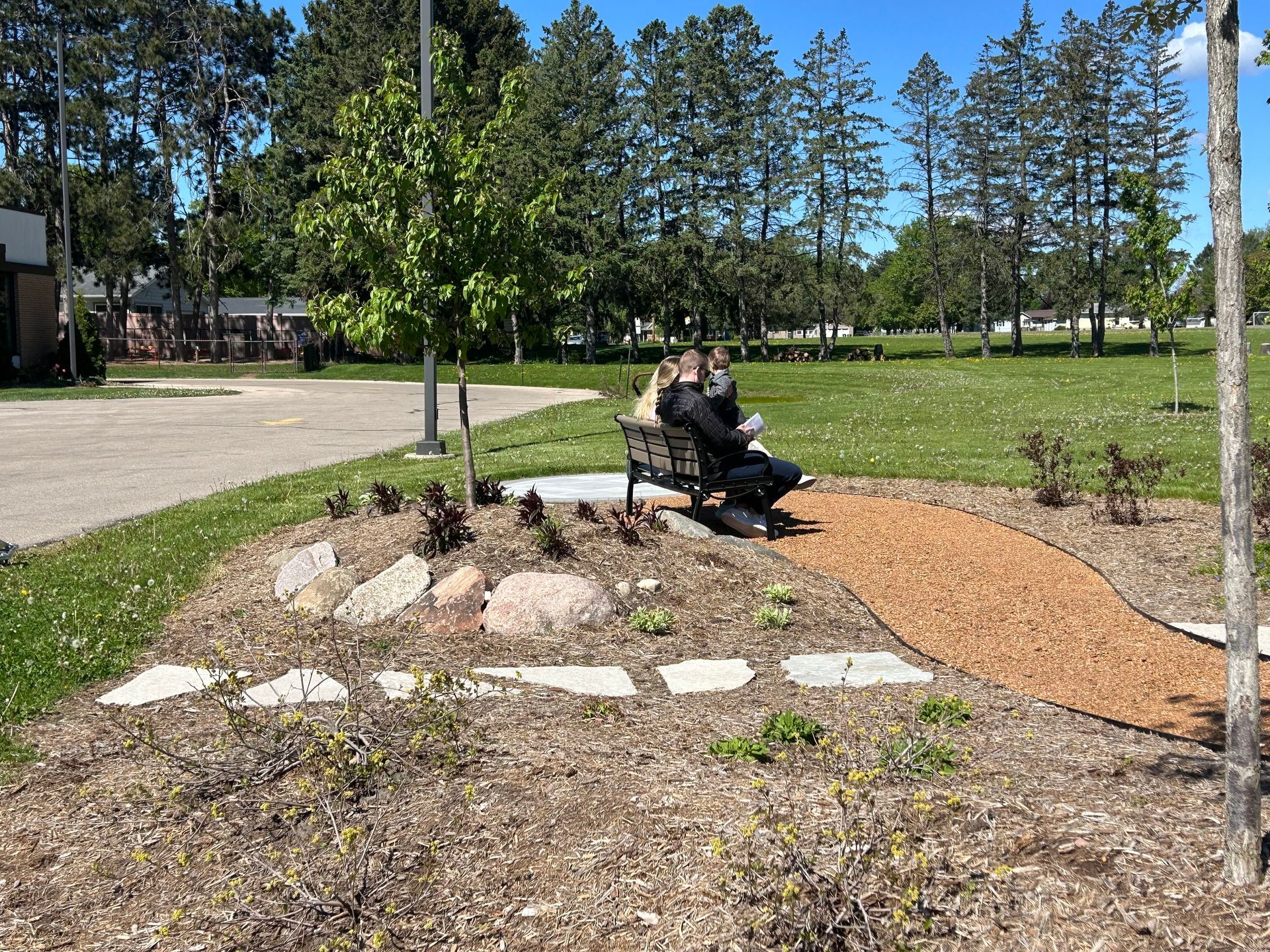 Person sitting on a bench beside a landscaped path in a sunny park