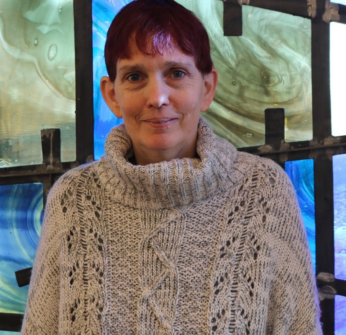 A woman with red hair is wearing a sweater and smiling