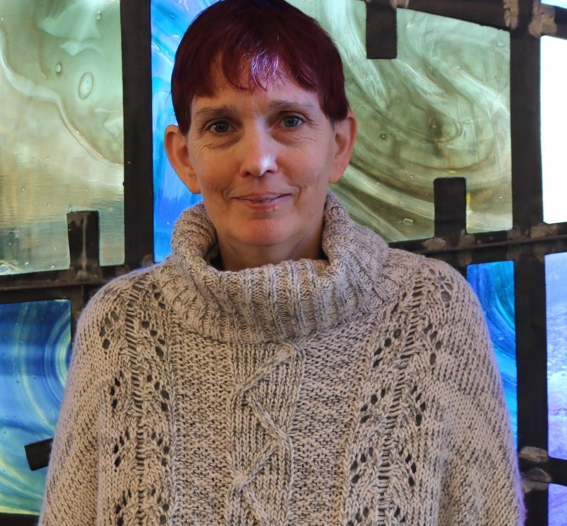 A woman wearing a sweater stands in front of a stained glass window