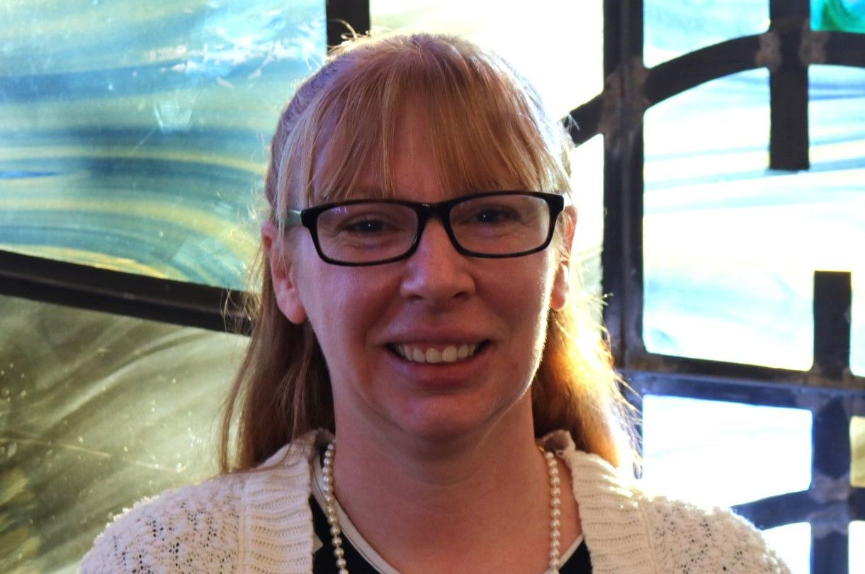 A woman wearing glasses and a pearl necklace smiles for the camera