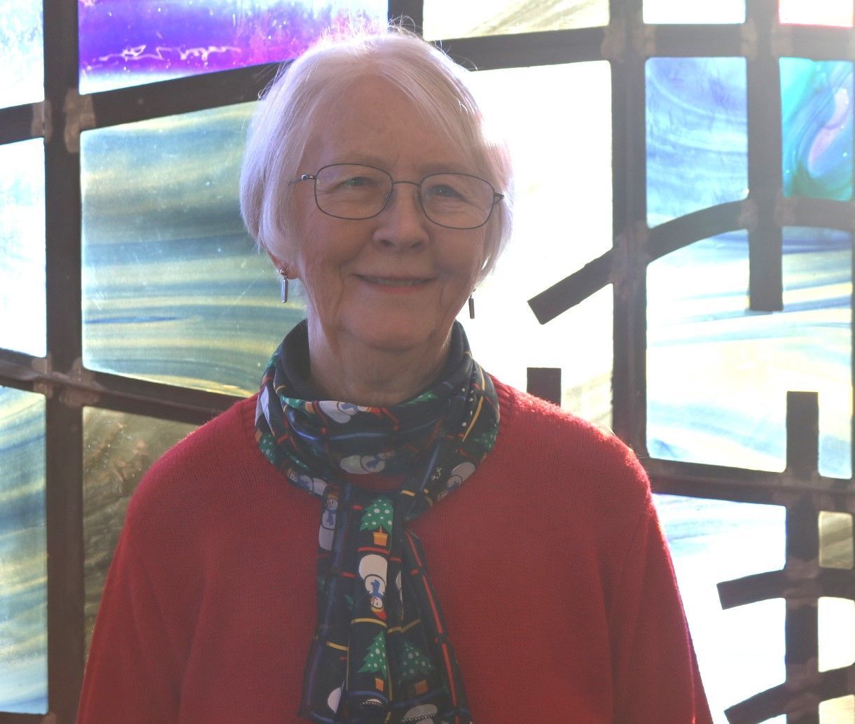 A woman wearing glasses and a scarf is standing in front of a stained glass window.