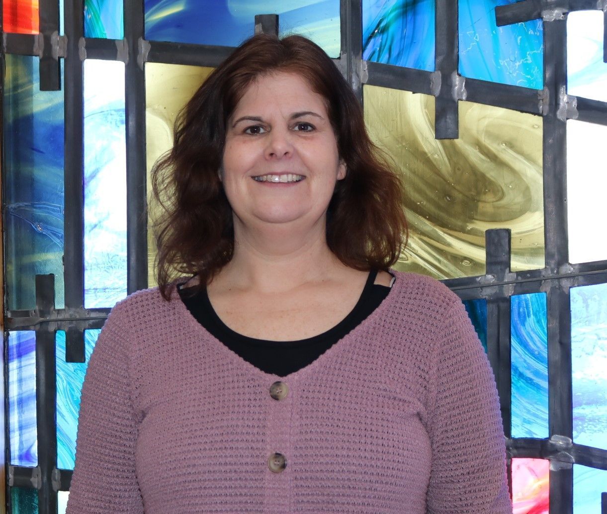 A woman is smiling in front of a stained glass window