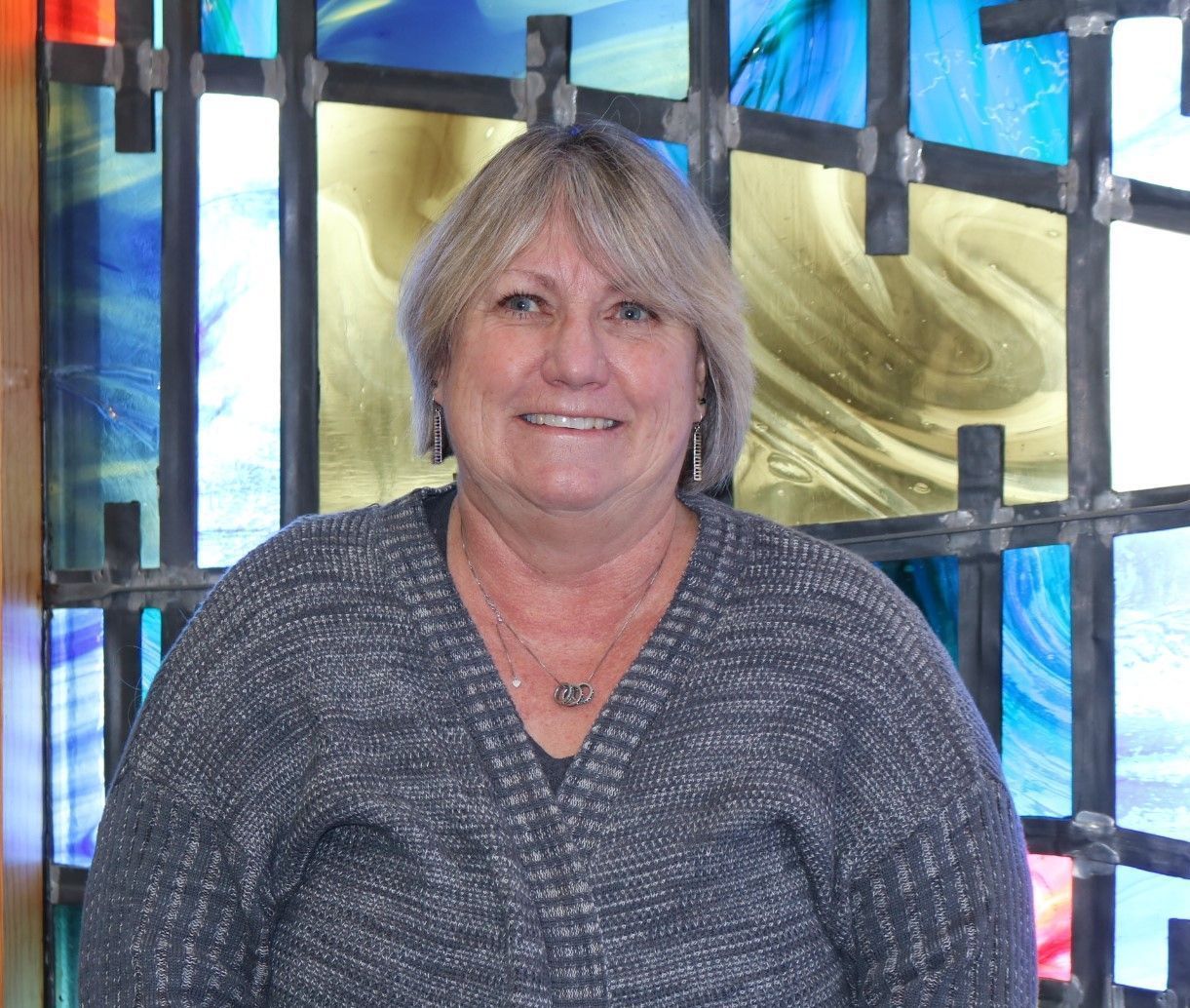 A woman is smiling in front of a stained glass window.