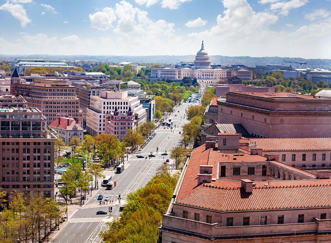 City avenue leading to the U.S. Capitol under a bright blue sky, with buildings and autumn trees along the road