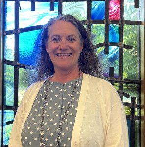 A woman is smiling in front of a stained glass window.