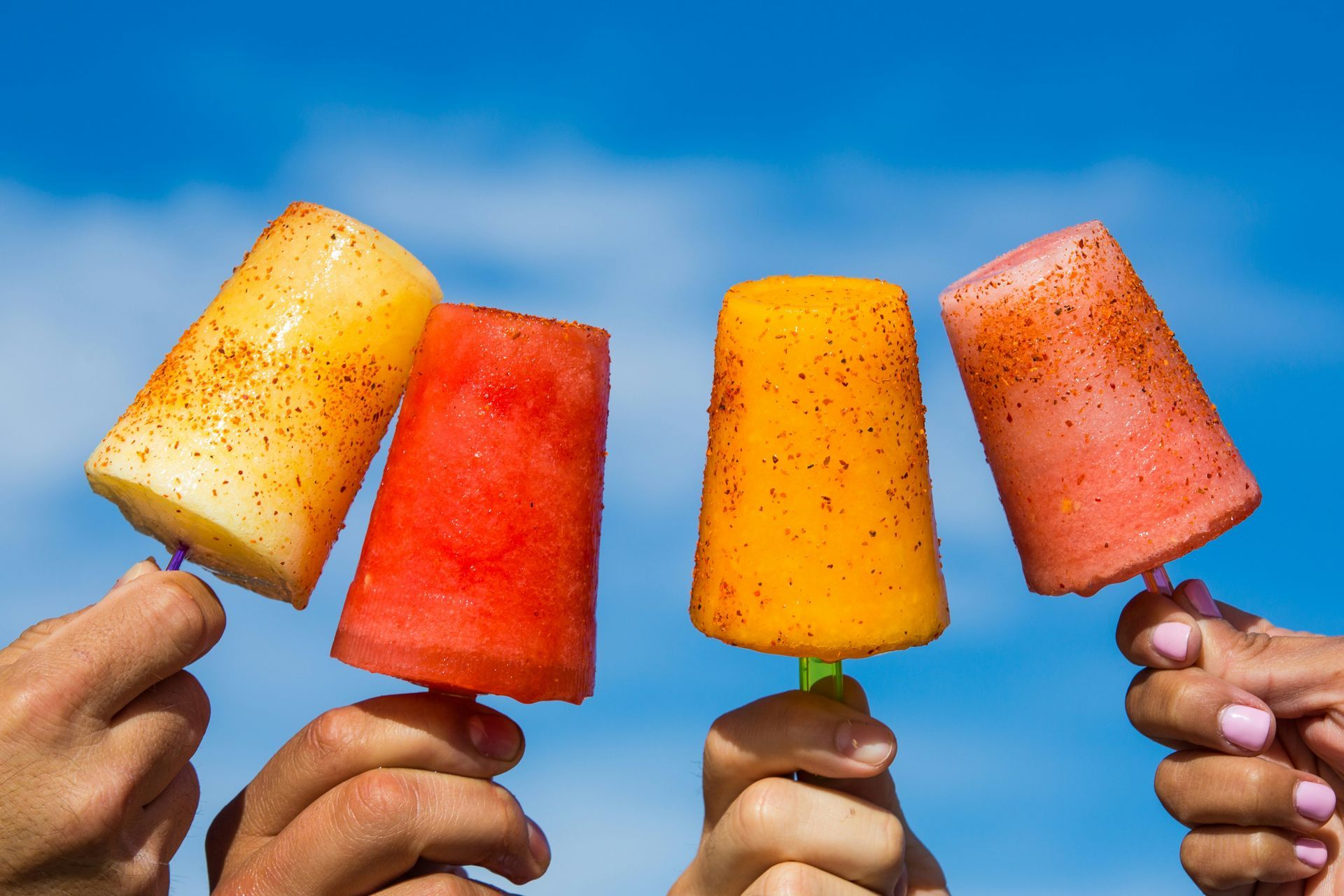 Four hands holding colorful popsicles against a bright blue sky