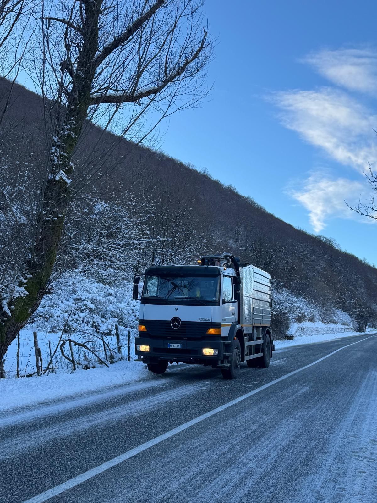 Un camion che percorre una strada di montagna innevata sotto un cielo azzurro.