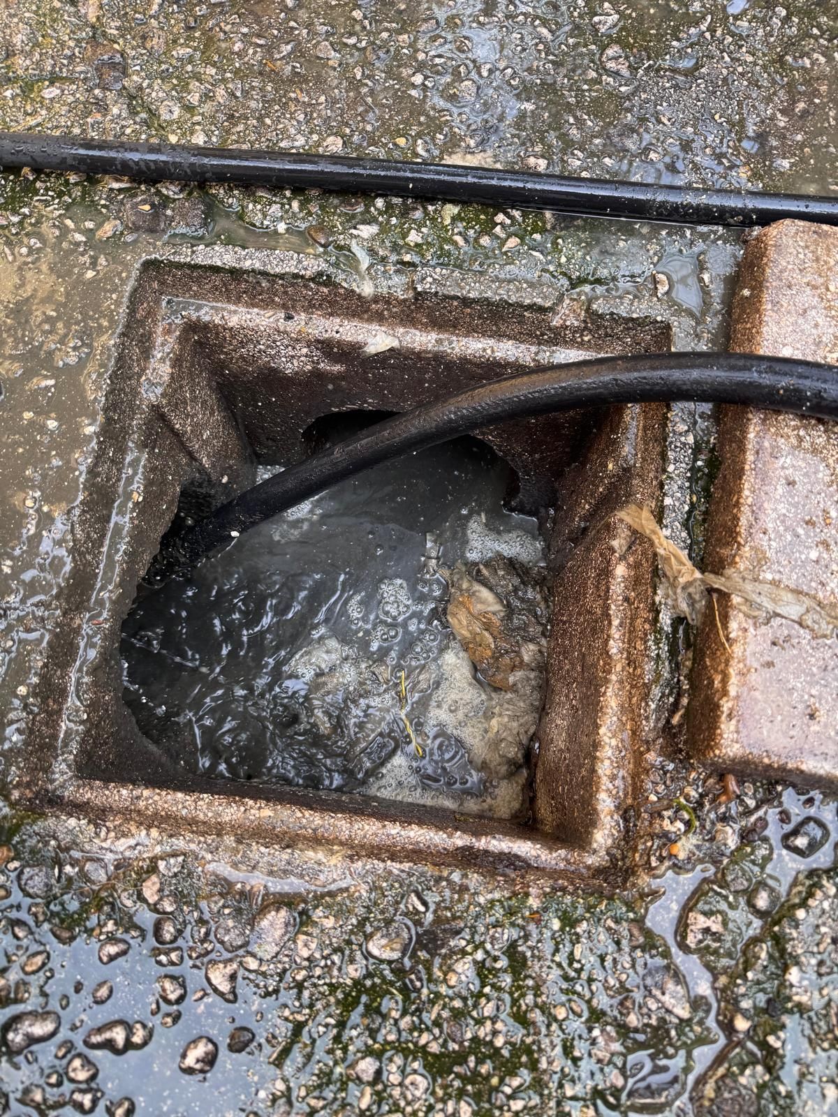 Acqua che scorre in uno scarico quadrato in cemento con un tubo nero su pavimentazione bagnata