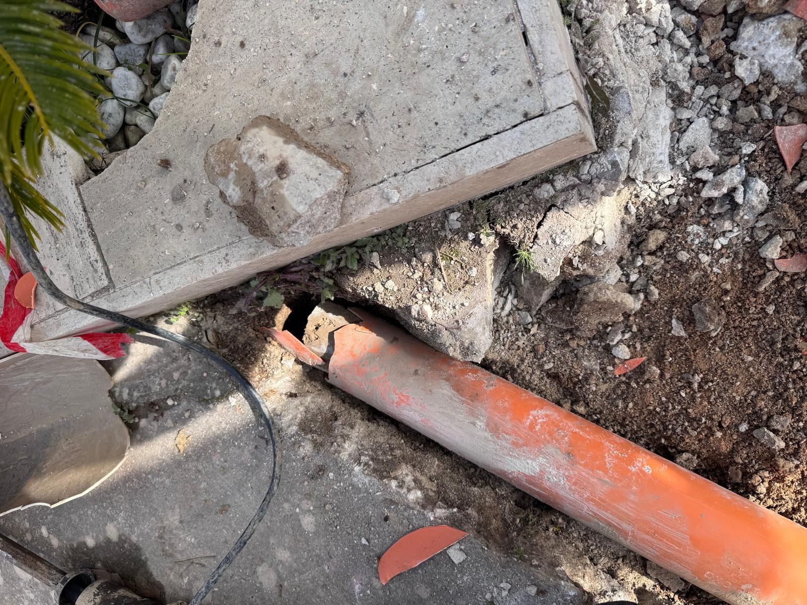 Un tubo arancione rotto accanto a una lastra di cemento su terra e macerie in un cantiere.