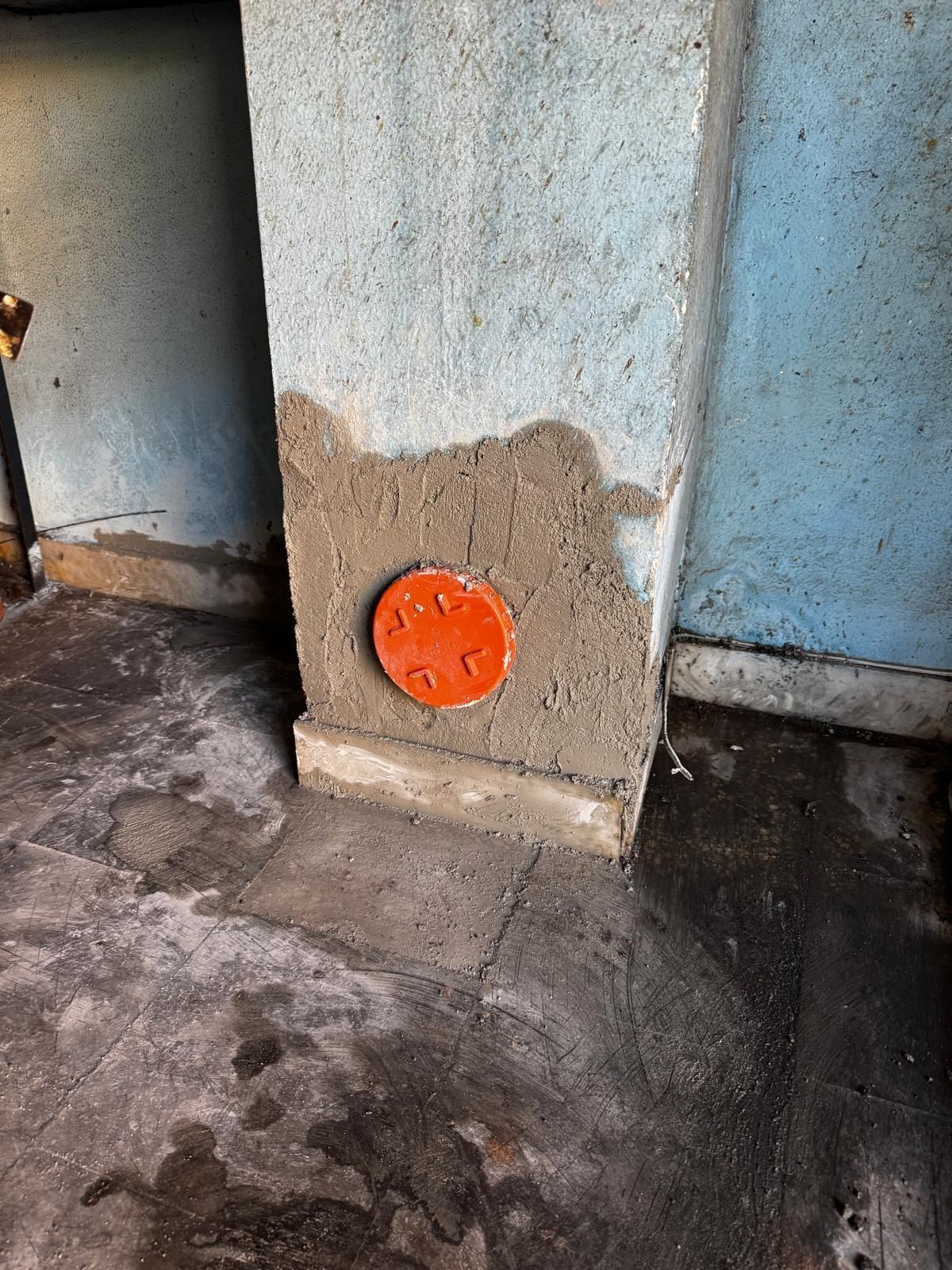Placca arancione per presa elettrica su un pilastro di cemento in uno spazio interno umido e poco illuminato