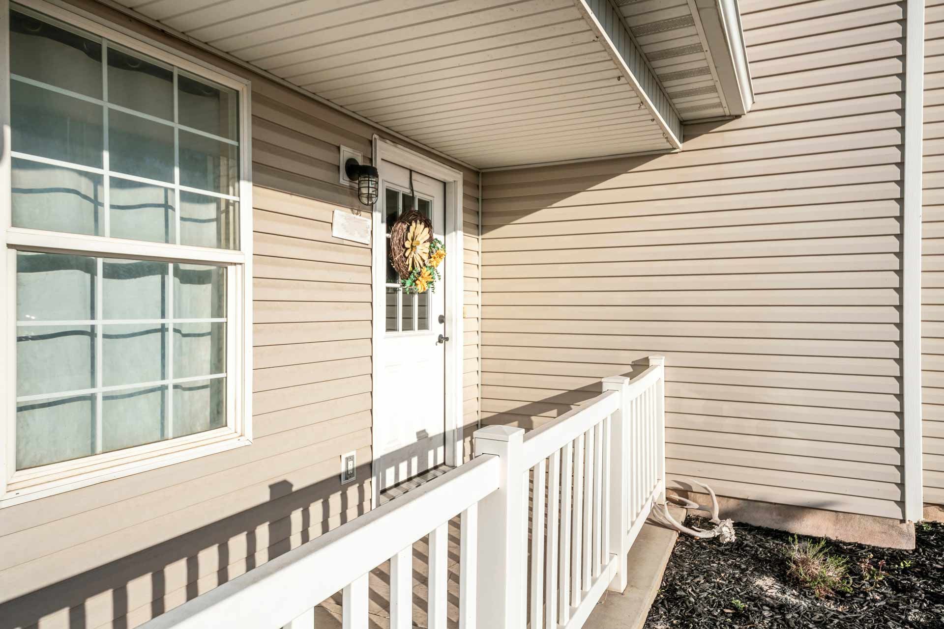 The front porch of a house with a white railing and a wreath on the door.