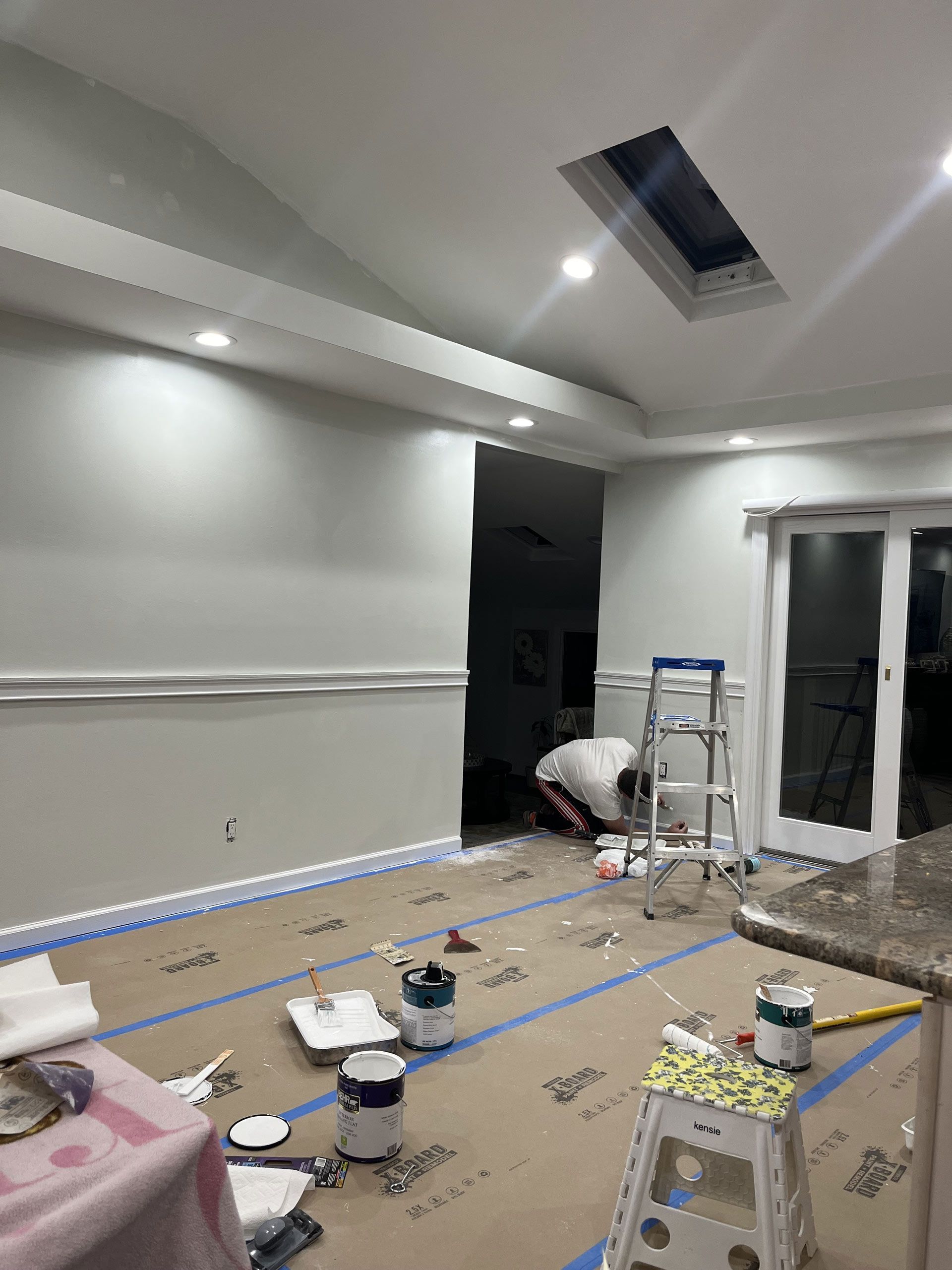 A man is painting a room with a skylight in the ceiling.