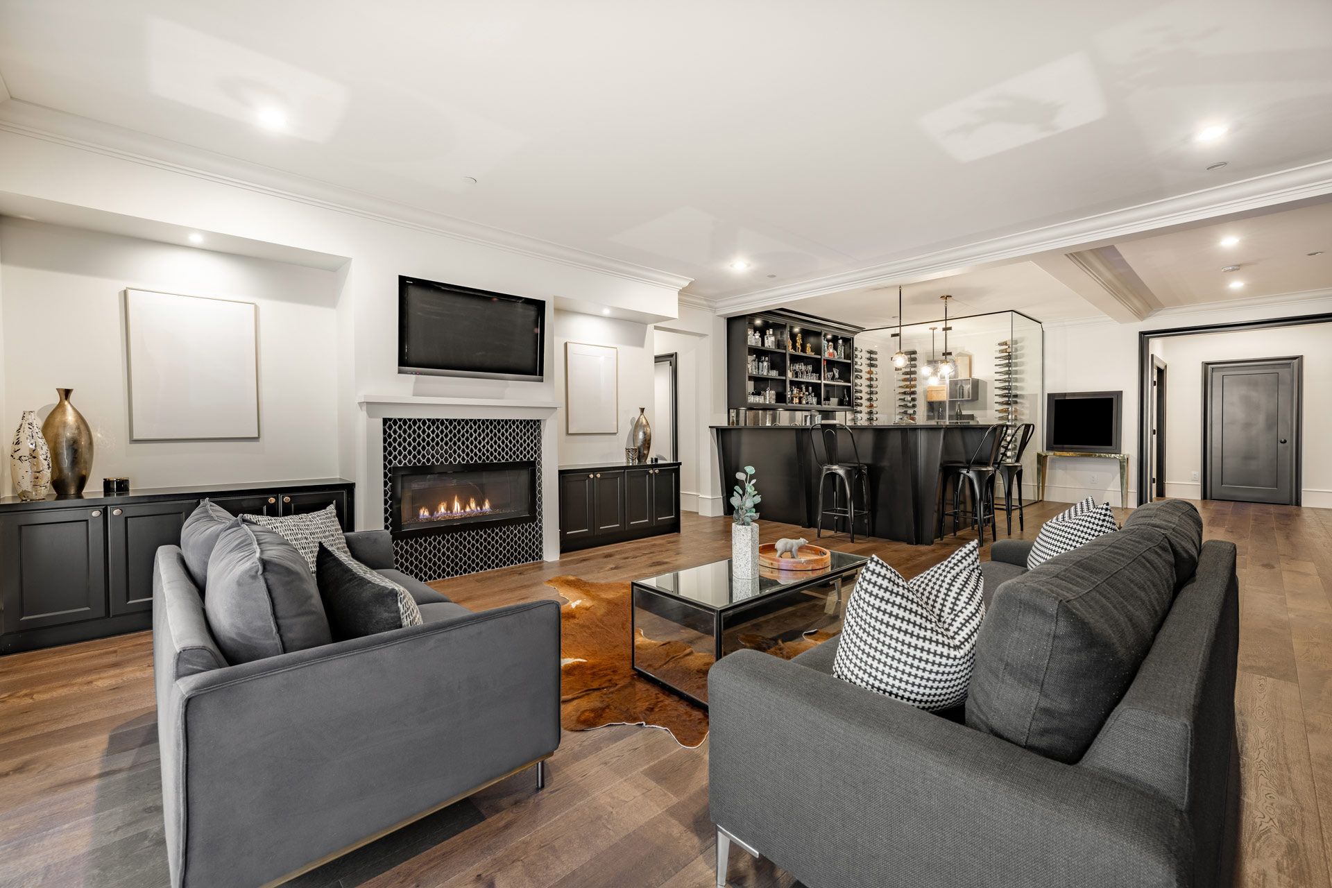 Living room with dark gray sofas, fireplace, bar, and hardwood floors.