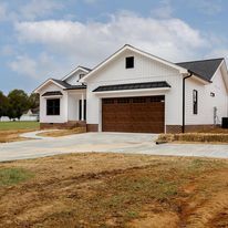 A white house with a brown garage door is sitting on top of a dirt field.