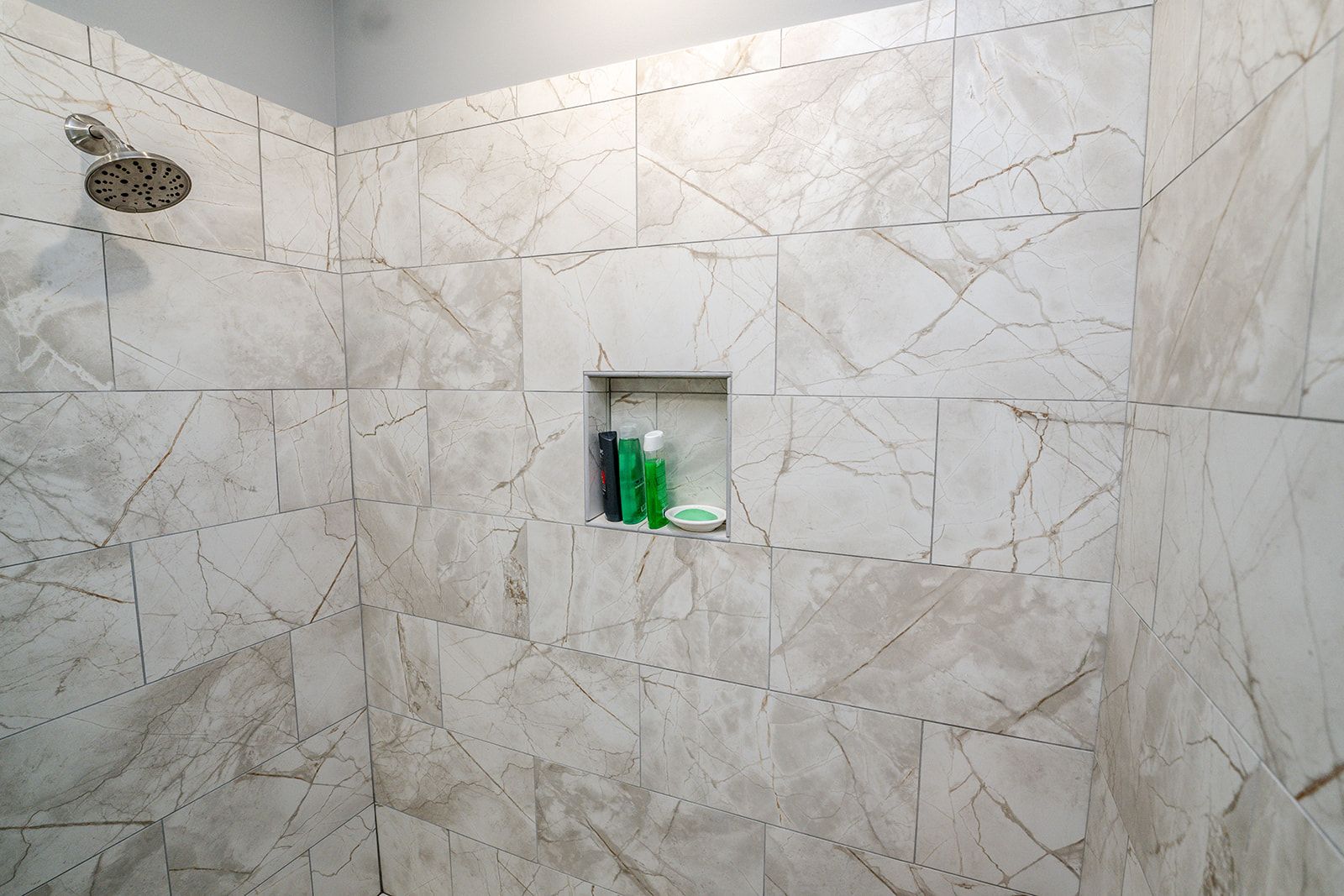 A shower with a soap shelf and a shower head.
