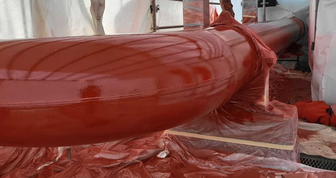 Freshly coated red pipe section prepared for pipeline maintenance and protective sealing.