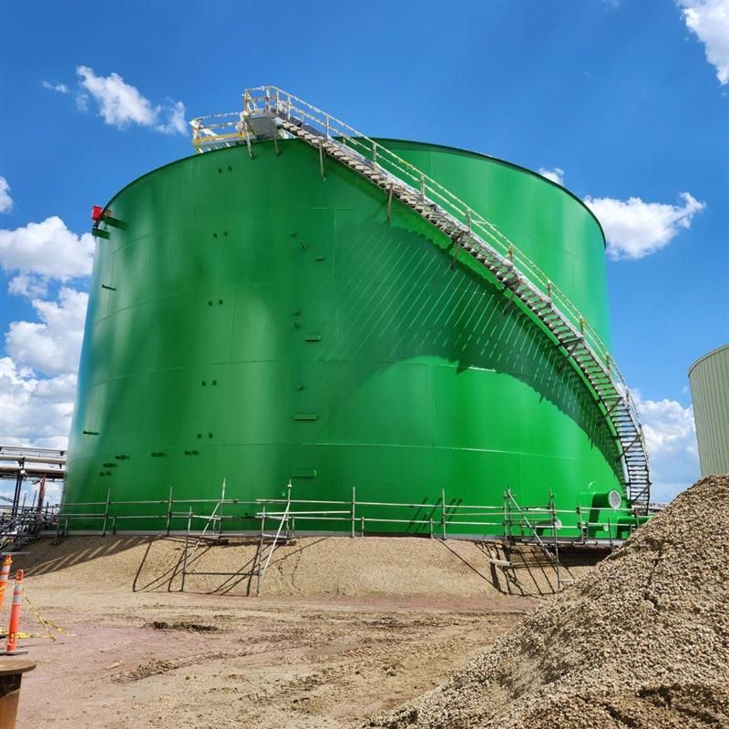 Large green industrial storage tank recently completed with professional tank painting, showing stair access under a blue sky