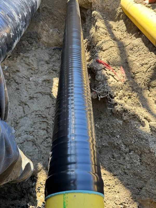 Close-up of a black-coated pipe laid in a trench during pipeline construction