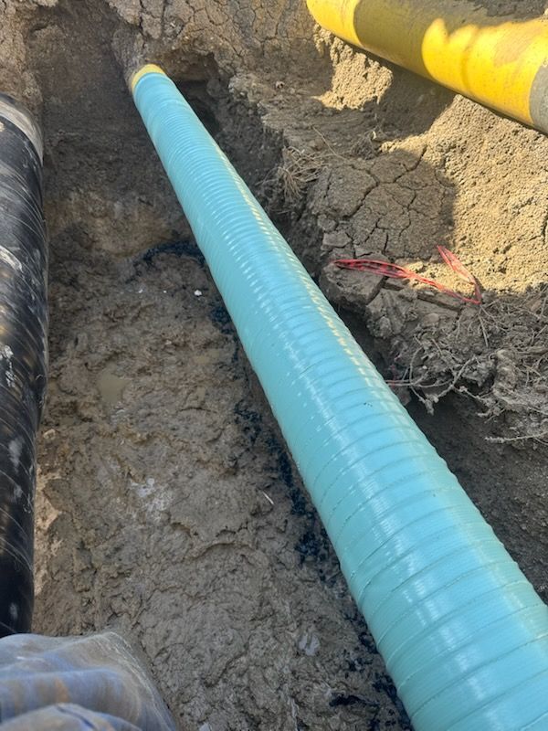 Pipeline construction showing freshly coated blue pipe laid in trench for underground installation