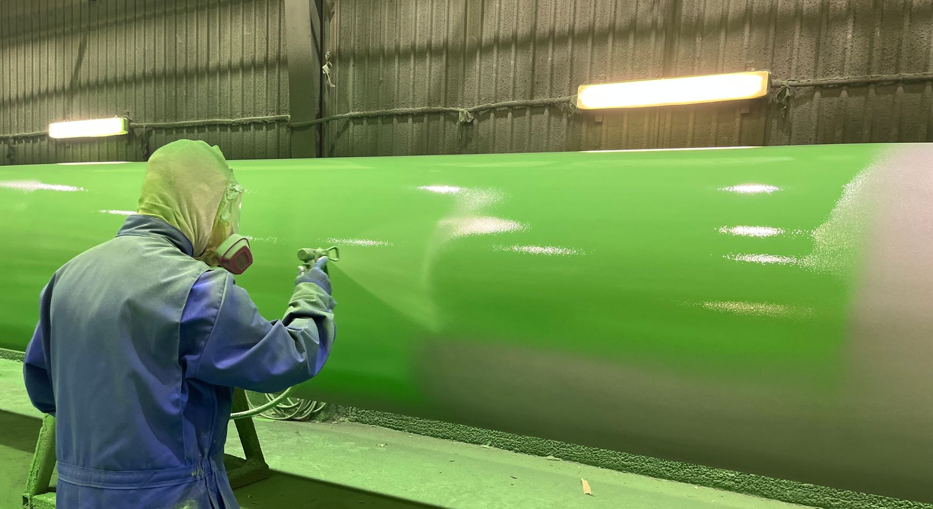 Technician spray painting a large pipe during pipeline maintenance inside an industrial facility.