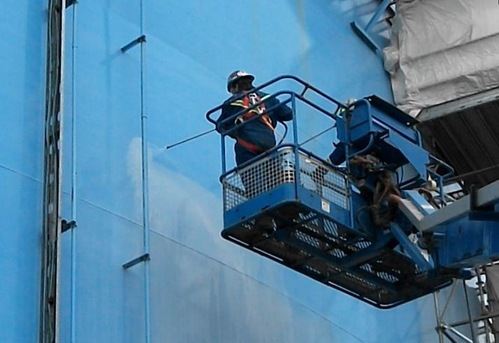 Industrial worker using spray system to apply protective coating during vertical tank painting